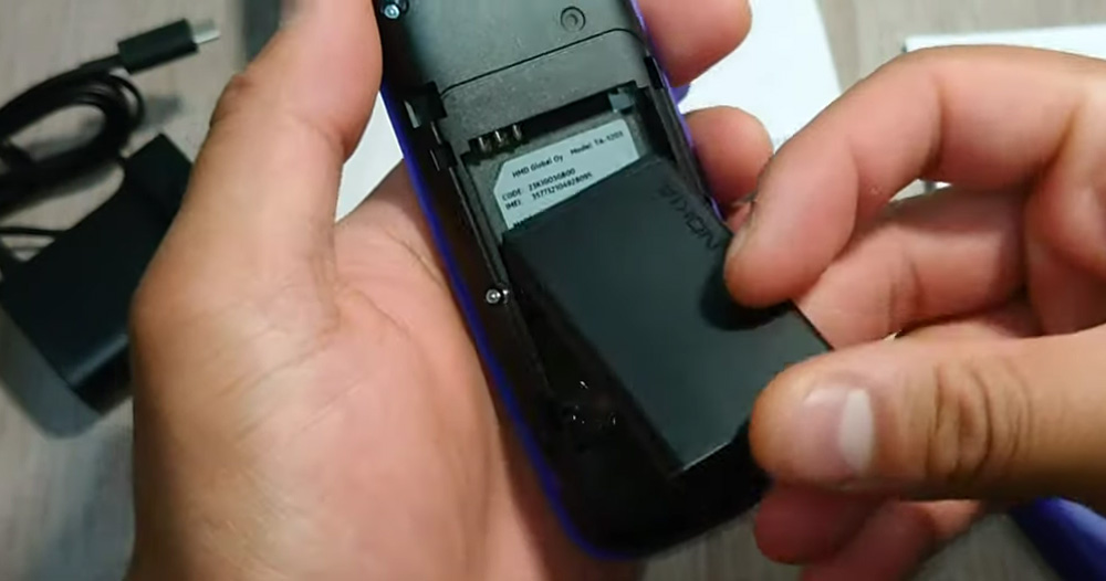 گوشی نوکیا 105 در دست قرار دارد و دست دیگر در حال نصب باتری روی گوشی است