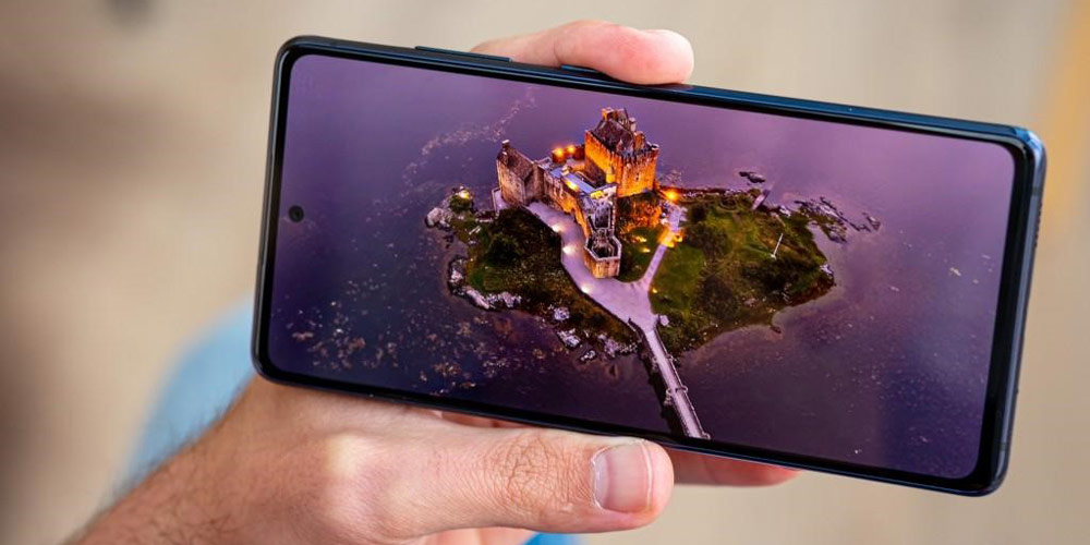 موبایل در دست و ال سی دی اس 201 اف ای سامسونگ تصویری یک قلعه در میان یک جزیره در اقیانوس را نمایش می دهد