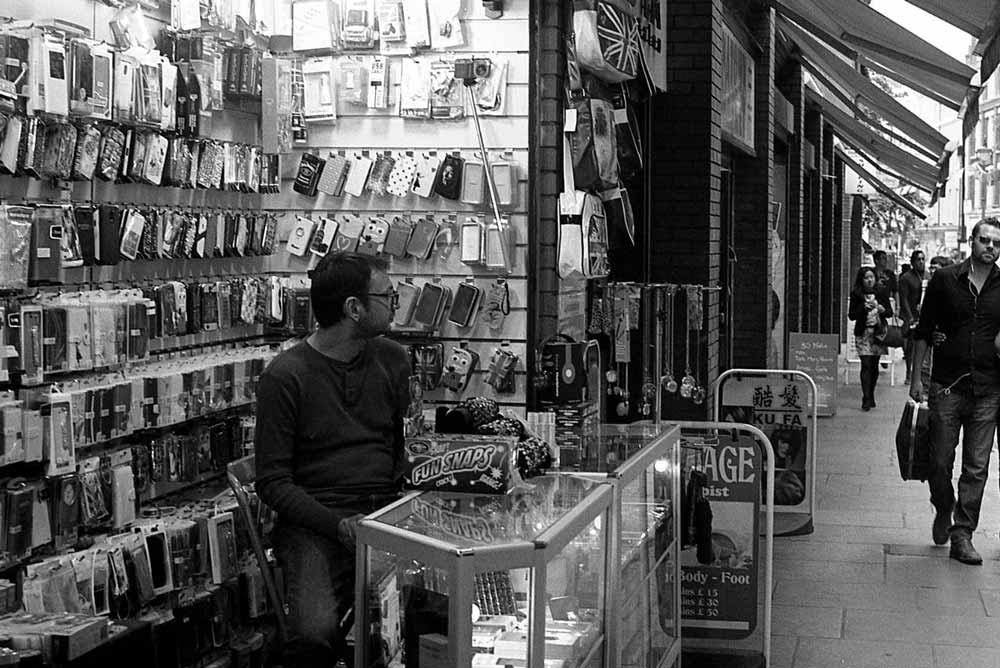 مرد در مغازه موبایل فروشی خود نشسته است
